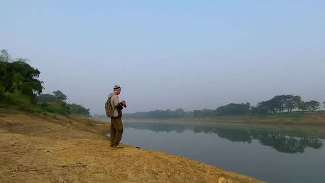 Wide shot of single male Photographer taking pictures of polluted river, dolly zoom in shot