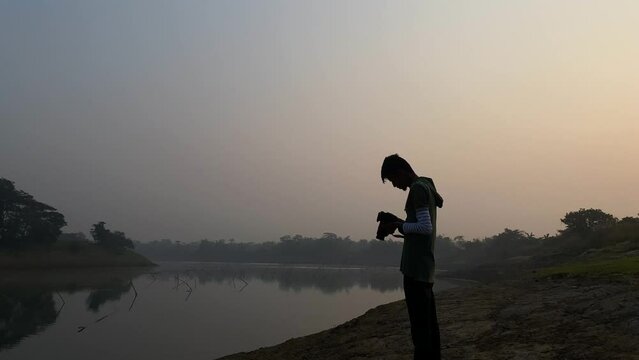 Photographer standing takes photos of river on a foggy winter morning, Sylhet