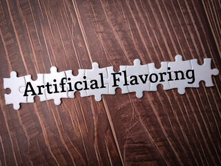 White puzzle with the word Artificial Flavoring on wooden background.