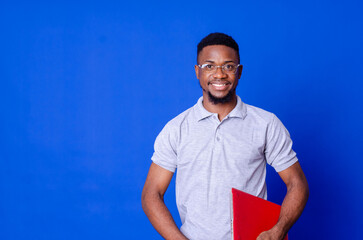 Young smiling african american man standing and using laptop computer isolated over blue background.