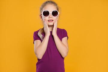 Emotional girl in stylish sunglasses on orange background