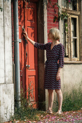 A woman stands outside the door of an abandoned house.