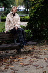 Fototapeta premium A woman sits on the back of a bench in the Park.
