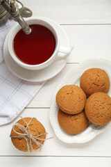 Delicious oatmeal cookies and hot tea on white wooden table, flat lay