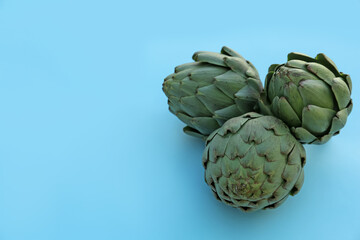 Obraz premium Whole fresh raw artichokes on light blue background. Space for text