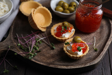 Delicious tartlets with red caviar and cream cheese served on wooden table, closeup