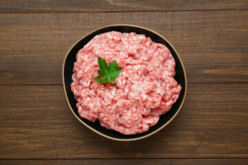 Bowl of raw fresh minced meat with parsley on wooden table, top view