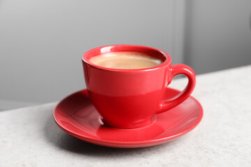 Red ceramic cup with hot aromatic coffee on white table indoors, closeup