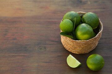 Fresh ripe limes and wicker basket on wooden table. Space for text