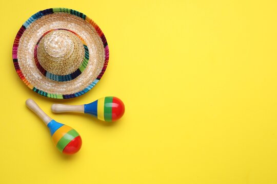 Colorful maracas and sombrero hat on yellow background, flat lay with space for text. Musical instrument