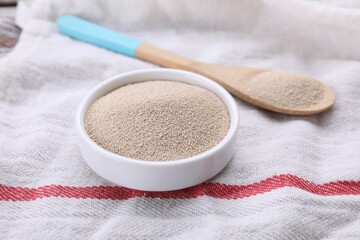 Bowl and spoon with active dry yeast on table, closeup