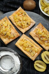 Fresh tasty puff pastry with sugar powder and kiwi served on grey table, flat lay