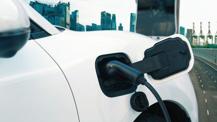 Electric vehicle, EV car recharges battery energy at charging station on the freeway in urban area...
