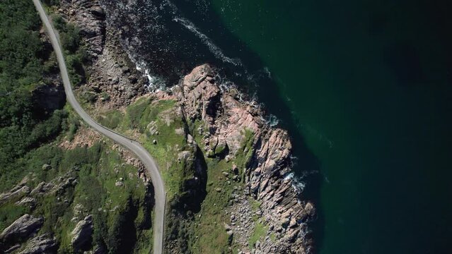 Aerial top down shot of a narrow dangerous Norwegian road along the coastline on a sunny day