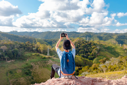 Traveler man sitting on top of a mountain and taking pictures or video with his professional camera of the landscape.