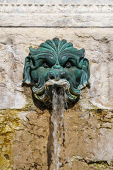 Fototapeta na wymiar Old metal fountain decoration of a face with water shooting from the mouth