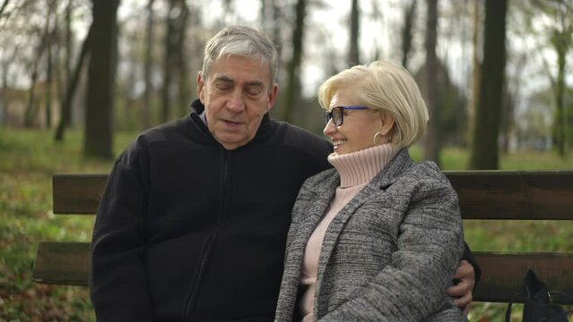Close-up shot of a loving mature couple talking while sitting on a bench in the forest park. Slow-motion shot