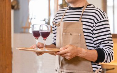 飲食店・バー・居酒屋・ワインバー・バル・ワインショップで赤ワインを持つ男性(ソムリエ・シェフ)