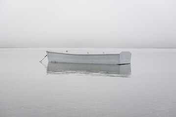 A dinghy floating in the ocean near shore on a foggy day.