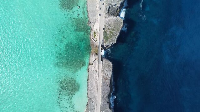 Cinematic aerial view descending top down drone shot of cars crossing glass window bridge on the island of eleuthera in the bahamas - separating the atlantic ocean from the caribbean sea