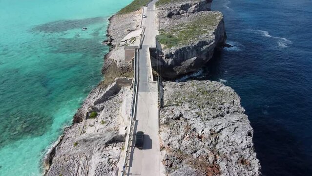 Cinematic aerial view drone shot following a car crossing glass window bridge on the island of eleuthera in the bahamas - separating the atlantic ocean from the caribbean sea