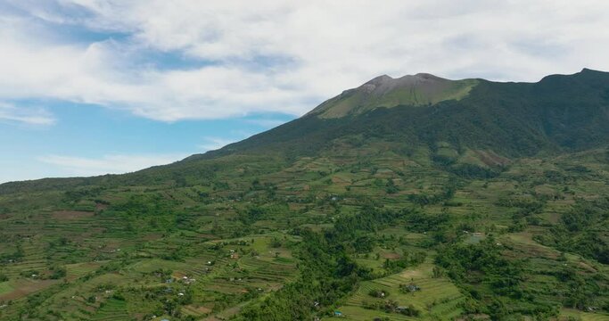 Aerial drone of farmland with plantings against a background of mountains and blue sky. Canlaon volcano. Negros, Philippines