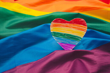 A rainbow heart shape symbol made from paper over the rainbow flag or LGBT flag