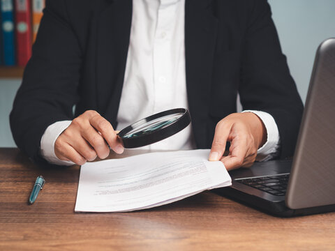 Close-up of a businessman's hand holding a magnifying glass and looking at reading documents while sitting at the tabl