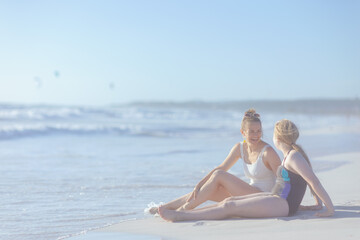 happy stylish mother and teenage daughter sitting at beach