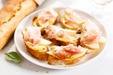 Obraz na płótnie Canvas Crostini with cheese, sliced pear and prosciutto on white plate.