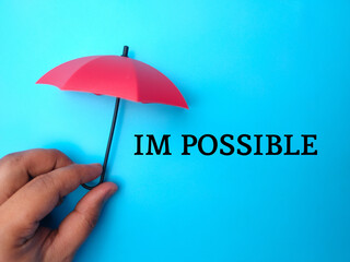 Hand holding red umbrella with the word IM POSSIBLE on blue background.