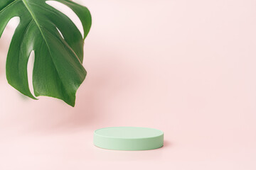 Round green podium next to monstera leaf against pink background.