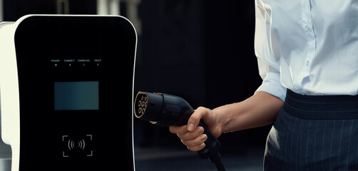 Focus EV charger plug and electric car at public charging station with blur progressive...