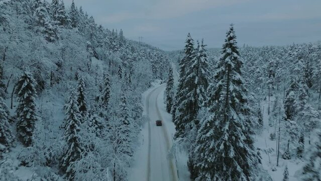Drone footage of an electric car (EV) driving in beautiful snowy landscape in Norway with snow covered tree tops