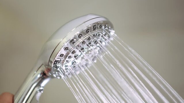 Male hand flips a switch on the running shower head to switch between the different jet settings. Close up shot