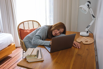 Portrait image of a young woman get tired and laying on the table while working on laptop computer at home