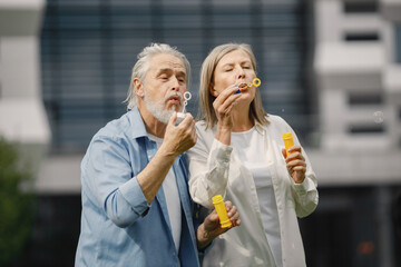 Senior couple standing on a grass in summer and blowing soap bubbles