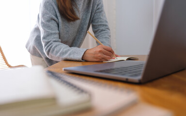Closeup image of a young woman writing on notebook while working or study on laptop computer at home