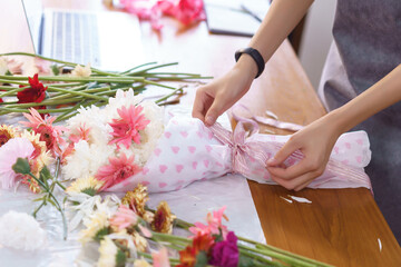 Obraz na płótnie Canvas Flower shop concept, Female florist creating colorful flowers bouquet with paper and ribbon bow