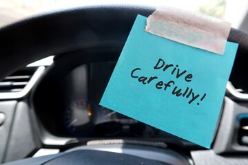 A blue paper note sticking on the car steering wheel, with text written DRIVE CAREFULLY, to remind...