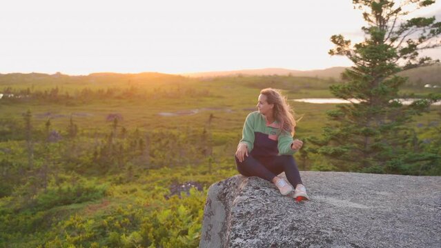 Woman sitting on rocks in the wilderness in golden hour sunset smiling