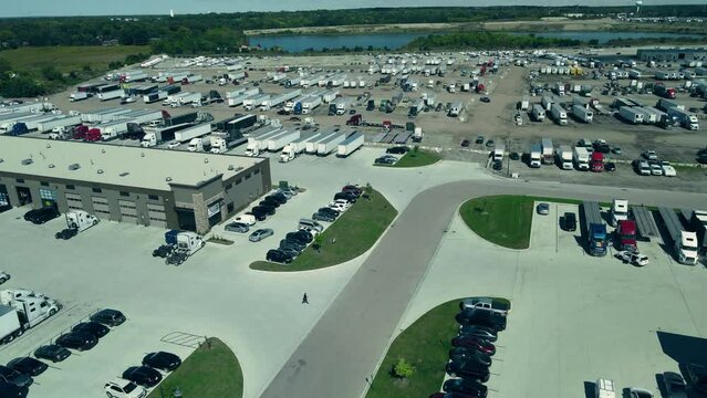 plaza of truck repair shops and parking lots full of reefers, dry vans, flatbets step decks. Location East Dundees, Illinois. Trucking industry aerial.