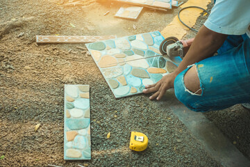 Hands of construction worker using an angle grinder for cutting the tiles at construction site. Man worker cutting beige tile with a circular saw. Cutting large ceramic tiles. Construction concept.
