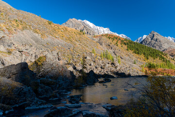 Part of an alpine lake near the stone shores in the shade against the backdrop of the mountains in Altai.
