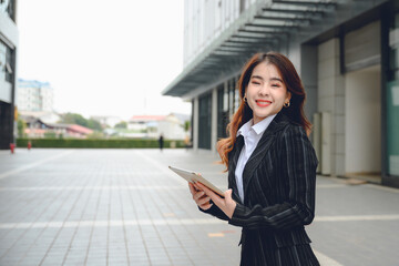 Portrait of Asian businesswoman in successful suit smiling happy looking at work on laptop close to her workplace Beautiful Asian woman holding tablet walking on outdoor street