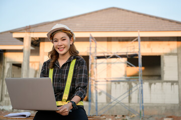 Asian woman engineer holding a laptop computer and a blueprint to plan about the construction site concept of working for success