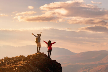 Couple two happy hikers stands with open arms at sunset view point high in mountains