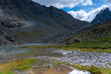 Fototapeta na wymiar Mountain lake with clear water Karakabak in the Altai mountains with snowy peaks and glaciers with under the clouds and green grass.