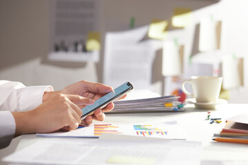 modern office desk at morning. businessman searches using smartphone. closeup