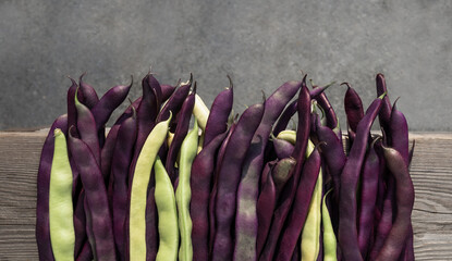 Beans on table. Vegetable harvest background or fall gardening concept. Top view of long raw purple and yellow beans on wooden board. Variety of Purple Peacock and Golden Wax Beans. Selective focus.